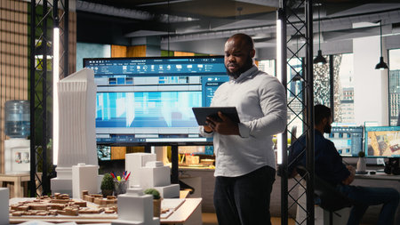 African american real estate developer reviews city planning layout on laptop, setting...
