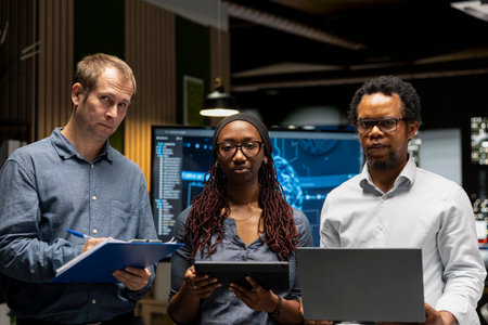 Portrait of programmers in office reviewing AI system metrics, monitoring performance dashboards. Technology company coworkers tuning neural networks using tools on devicesの写真素材
