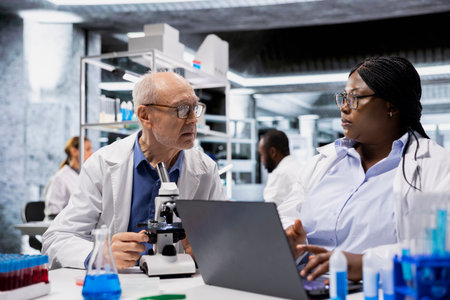 Senior scientist teaching intern to examine bacterial cultures using microscope. Elderly researcher...