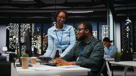 Business manager and assistant monitoring data analytics in dark office, utilizing reports and insights to plan forecast for performance metrics and statements. Goal setting late at night.の写真素材