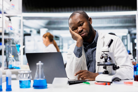 Lab researcher frowning, disappointed by experiment results data. Stressed african american man upset by inconclusive study results and research progress when documenting findings on laptopの写真素材