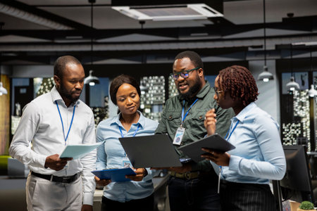 Group of black workers collaborating on project strategy and briefing, using data from charts on gadgets to drive performance metrics. Fostering teamwork and a workplace partnership.の写真素材