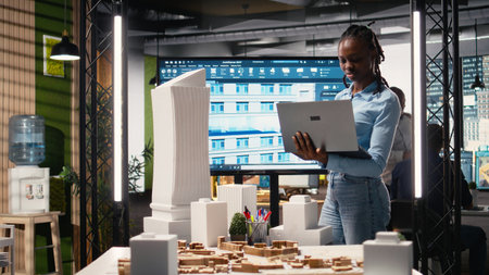 African american male developer examines detailed construction blueprints and layout details, documentation for project approval on a residential property project in a urban area.の写真素材
