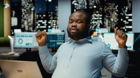 African american male worker stretching his back and neck muscles, correcting posture for muscle relief and relaxation. Strain and neck stiffness due to intense activity in office.の写真素材