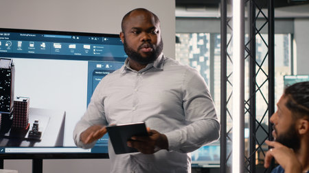 Black contractor reviewing architectural software and 3D models with his team in office, successful residential project for urban development. Smart city housing for infrastructure growth.の写真素材