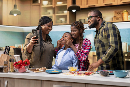 Mother takes selfies on phone while they cook delicious homemade pizza together in modern kitchen,...