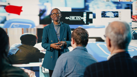 African American female speaker delivers powerful media presentation at tech conference, diverse audience in modern conference hall. Young adult discusses advertising and public relations.の写真素材