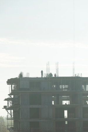 Ironworkers install vertical steel bars on new building roof edge during sunny day. Men in...