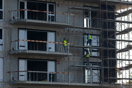 Close up of construction workers standing on metal scaffolding to install insulation on concrete...
