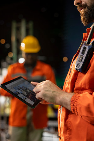 Close up of offshore platform engineer checking equipment status indicators on tablet system...