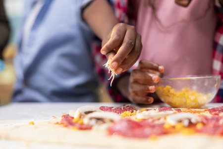 Close up of african American children adding grated cheese and mozzarella, sharing pizza day at home and learning to cook with their parents for bonding time. Togetherness and laughter.の写真素材