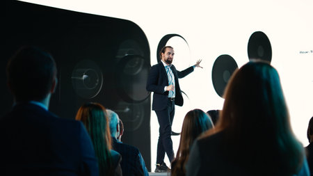 Male CEO presenting new mobile phone product launch on stage with premiere of modern smartphone interface. Entrepreneur introduces innovation and development with product release.の写真素材