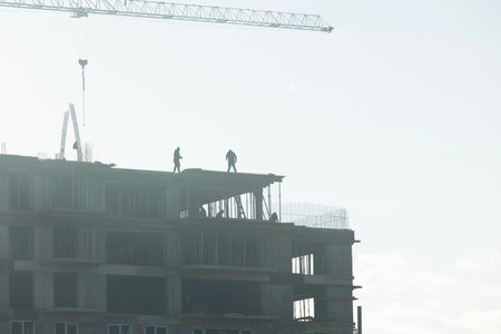 Contractors in construction site using heavy machinery to rise new building during sunny day. Crane...