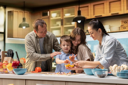Family in the kitchen enjoy cooking together and preparing homemade pizza with toppings. Parents and two children sharing laughter and quality bonding time with a delicious meal.の写真素材