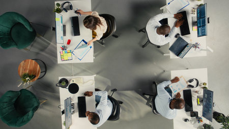 Top down view of colleagues sharing reports and visual data on computer. Work team performs risk...