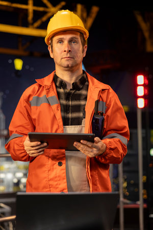 Portrait of engineer working on offshore oil rig platform late at night, analyzing drilling...