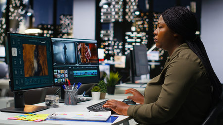 Woman video creator working on editing a movie montage project, multitasking with dual monitors. Female footage editor starting the cinematic creative process, film editing industry. Camera B.の写真素材