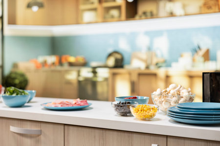 Modern kitchen setup with pizza ingredients on a countertop. Bowls of corn, olives, mushrooms and...