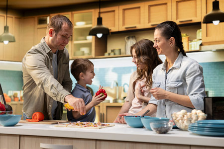 Family of four preparing a delicious homemade pizza together, enjoying fun weekend activity in the...