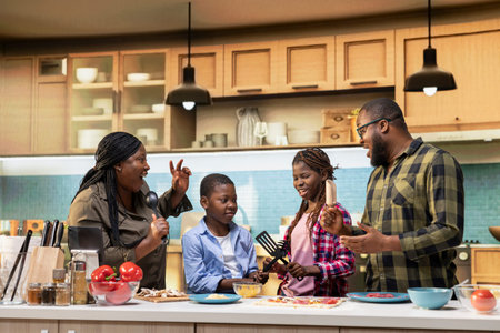 African American family enjoying silly karaoke session for pizza day in the kitchen, singing with...