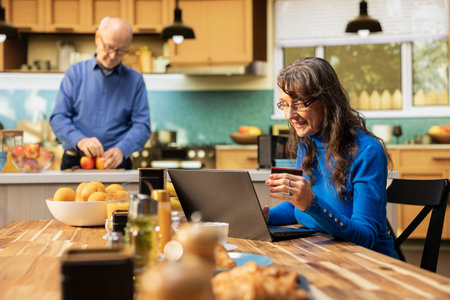 Elderly woman doing online shopping with a credit card in hand, reviewing list of groceries and daily essentials in e-commerce app cart on laptop. Female shopper checks credentials for order.の写真素材