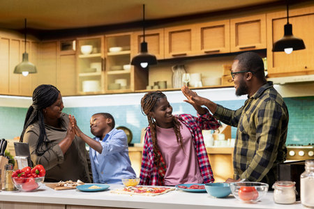 Black family sharing high five and clapping hands after finishing homemade pizza in the kitchen....