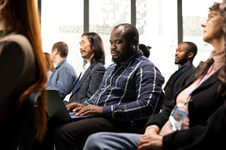 Black businessman takes notes on laptop at professional summit, forum conference with panel discussion and public speaker. Multiracial audience listen to ideas for entrepreneurship.の写真素材