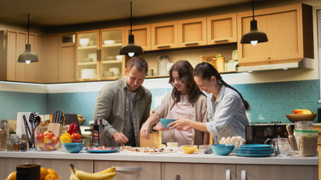 Parents and tween girl laughing while sprinkling mozzarella on pizza in the kitchen, family scene shows bonding time. Culinary creativity and homemade food preparation together.の写真素材