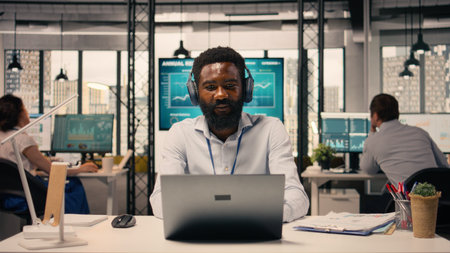 Cheerful black man listening to audio playlist on wireless headphones, reviewing charts and graphs...