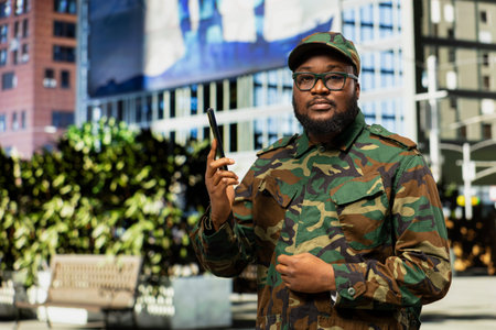 Portrait of military officer using telephone call line for patrol orders in the city center, walking along a downtown street wearing tactical camouflage uniform. Honor, courage and readiness.の写真素材