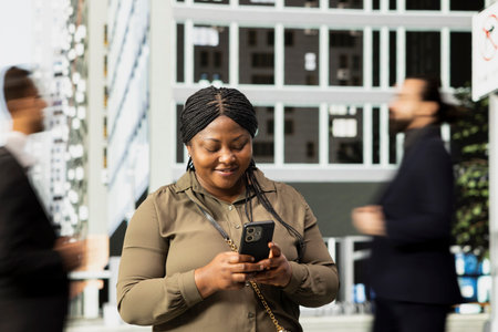 African american female adult browsing phone apps in the metropolitan area, walking among constant...