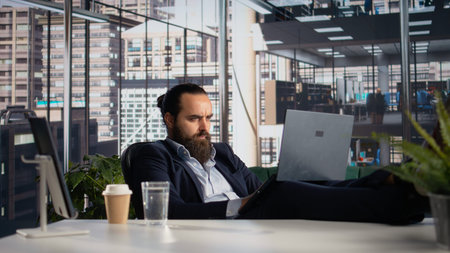 Male CEO sitting in his chair laid back and solving tasks on laptop, goal oriented leader ensures...