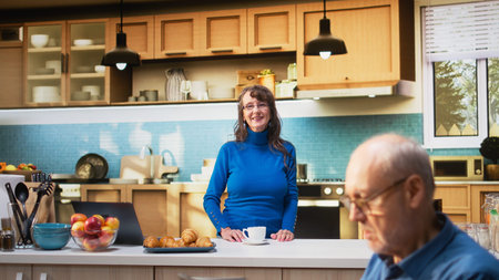 Portrait of senior woman smiling in the kitchen and enjoying cup of warm drink. Natural portrait of retired life captures peaceful lifestyle moments and the domestic comfort of home. Camera A.の写真素材