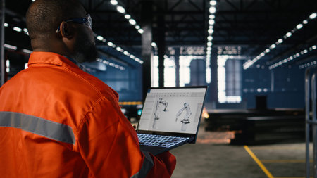 African american technician reviews robot software model on laptop in manufacturing plant,...