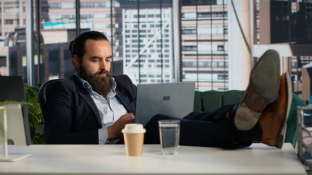 Adult businessman laid back working comfortable on laptop for daily tasks, dedicated on management planning work. Male at desk stretching, checking data and insights for productivity.の写真素材