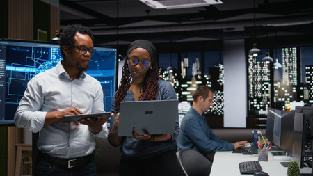 Tech agency colleagues collaborating to optimize AI performance in office late at night. Software...