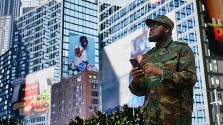 Black military service person browses website on a smartphone in the city center, professional uniform, integrity and calm attitude reflecting loyalty and mission focus while on patrol. Camera A.の写真素材