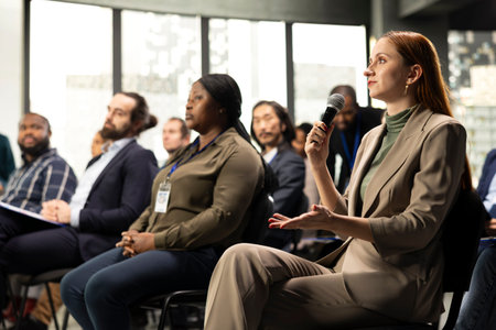 Young adult businesswoman in audience interacting with presenter, asking questions and engaging in...