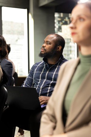 African american businessman using laptop and paying attention to presentation in conference room, working on his pc and taking notes. International convention summit with diverse staff.の写真素材