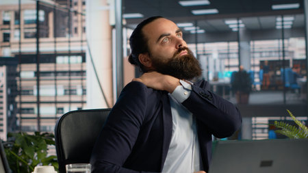 Male professional with backache and muscles strain due to bad chair posture, stretching his lower back and neck muscles. Business man weary with physical fatigue and stiffness, workload.の写真素材