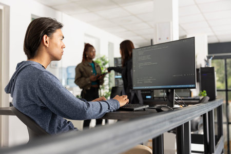 Focused software programmer works in diverse office, ensuring smooth web development. Young adult...