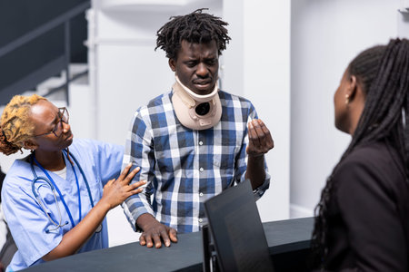 Injured patient checks appointment details at reception as female healthcare staff provide...