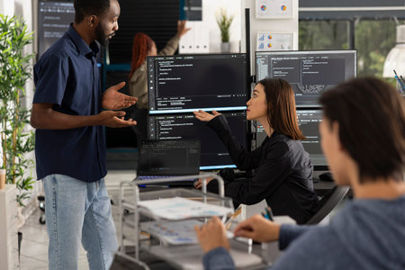 Group of developers sits around computers, discussing source code and system information during work...