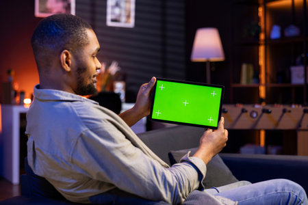 African american male freelancer holding tablet with mockup copy space screen, relaxing on sofa in a...