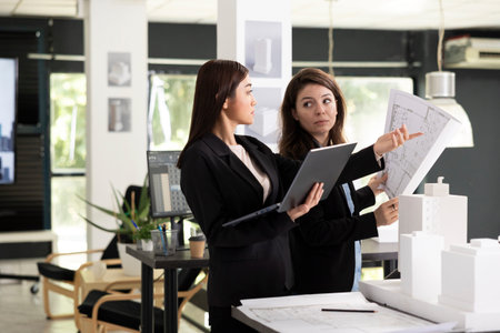 Female professionals compare digital and printed architectural designs, identifying necessary...