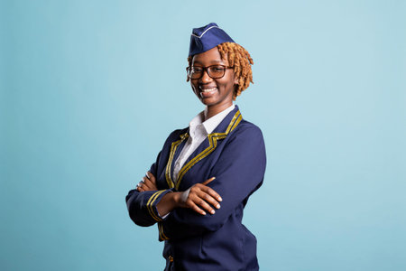 Smiling female flight attendant in blue uniform posing against isolated background. Confident and friendly air hostess looking at camera with arms crossed, ready to serve global travelers.の写真素材
