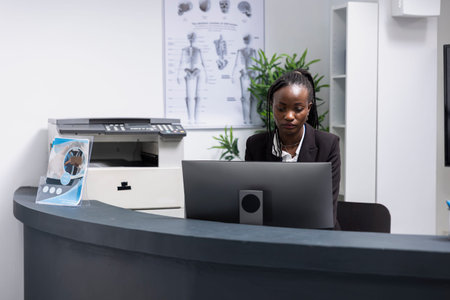 African american woman works at modern clinic reception desk, prepared to assist with patient...