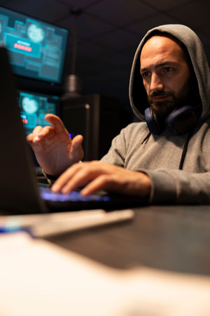 White man analyzing software solutions, coding and planning secure digital workflows. Caucasian male coder wearing sweatshirt hoodie, types steadily while reviewing technical interfaces on laptop.の写真素材