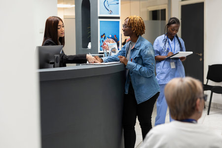 Friendly receptionist at front desk assists patient with updating health records and scheduling...
