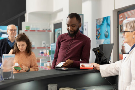 African american man pays for pharmacy items using smartphone, demonstrating cashless payment...